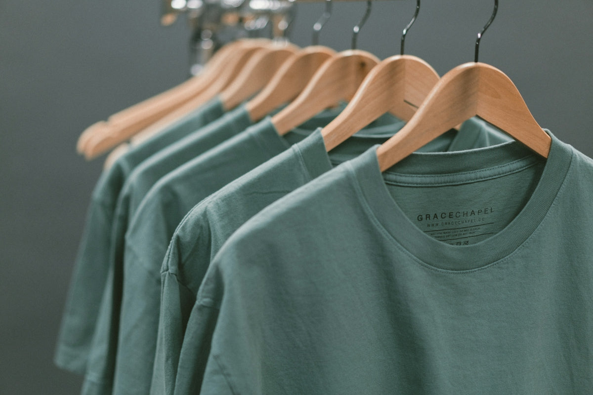 A row of green t-shirts hanging on wooden hangers against a grey background